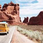 A yellow camper van on a road through a red rock canyon.